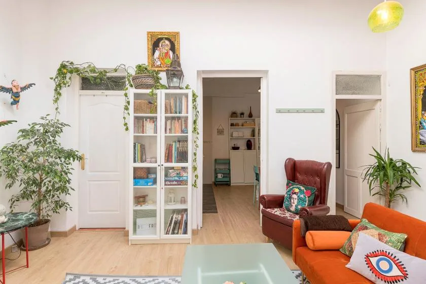 A bright living room with seating, a glass table, and tall shelving.