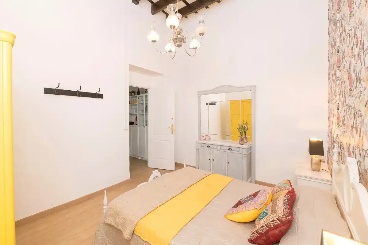 A bright bedroom with a bed, a dresser, and a doorway.