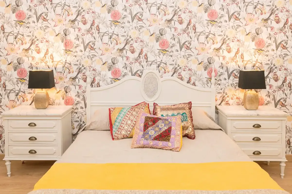 A bedroom with a bed, colorful pillows, and floral wallpaper.