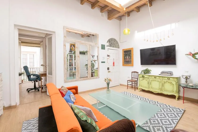A bright living room with orange seating, a glass coffee table, and a wall-mounted television.