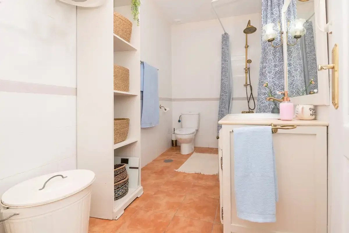 A bright bathroom with a shower, sink, and terracotta-colored floor.