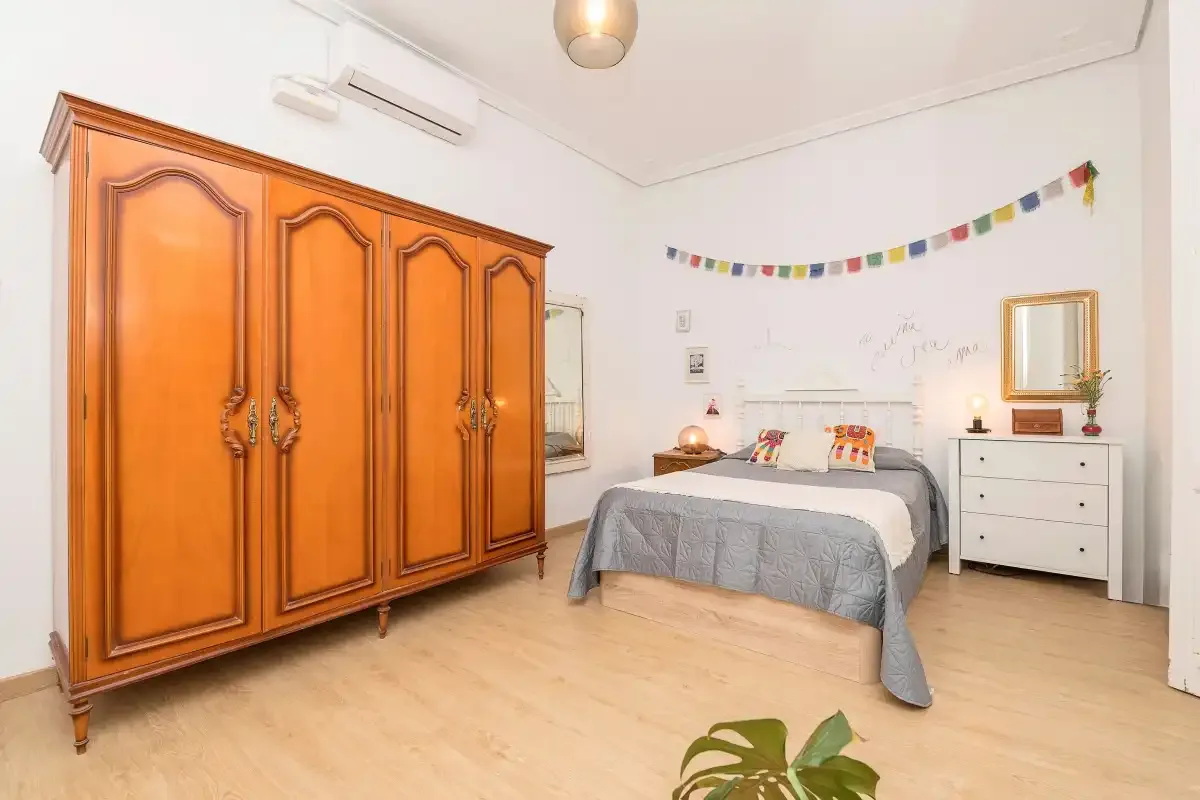 A bedroom with a large wooden wardrobe beside a bed.