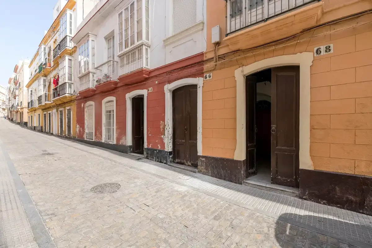 A cobblestone street runs past colorful multi-story buildings with balconies.