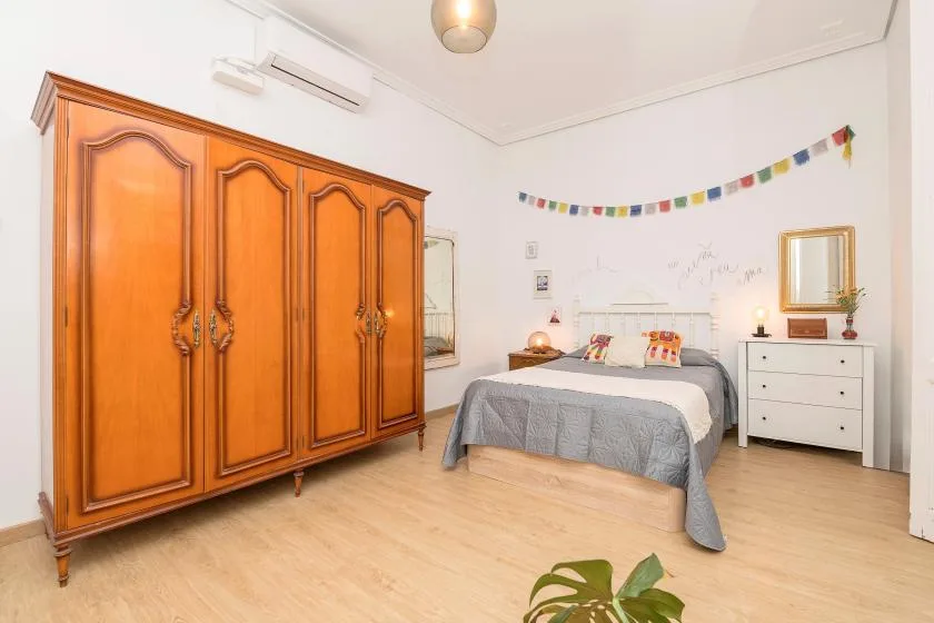 A bedroom with a large wooden wardrobe beside a bed.