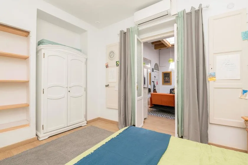 A bedroom with a white wardrobe, gray curtains, and colorful bedding.