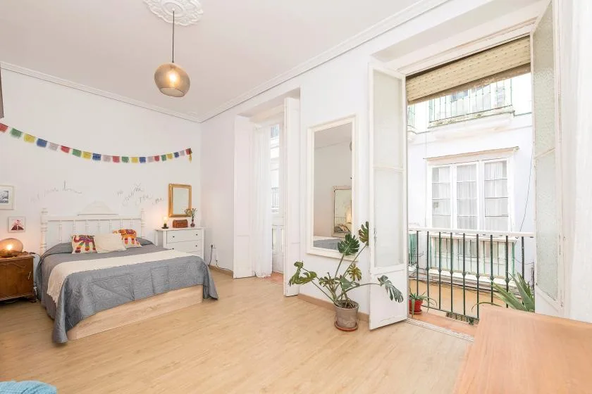 A bright bedroom with a bed and a large window opening onto a balcony.
