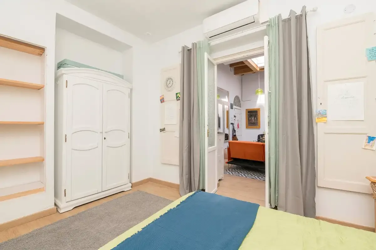 A bedroom with a bed in the foreground and an open doorway between gray curtains.