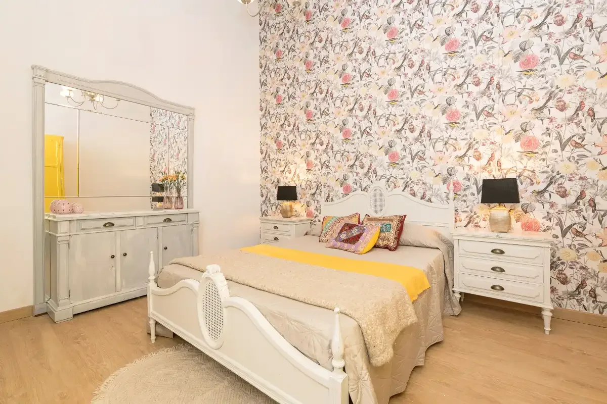 A bedroom with a white bed and floral wallpaper.