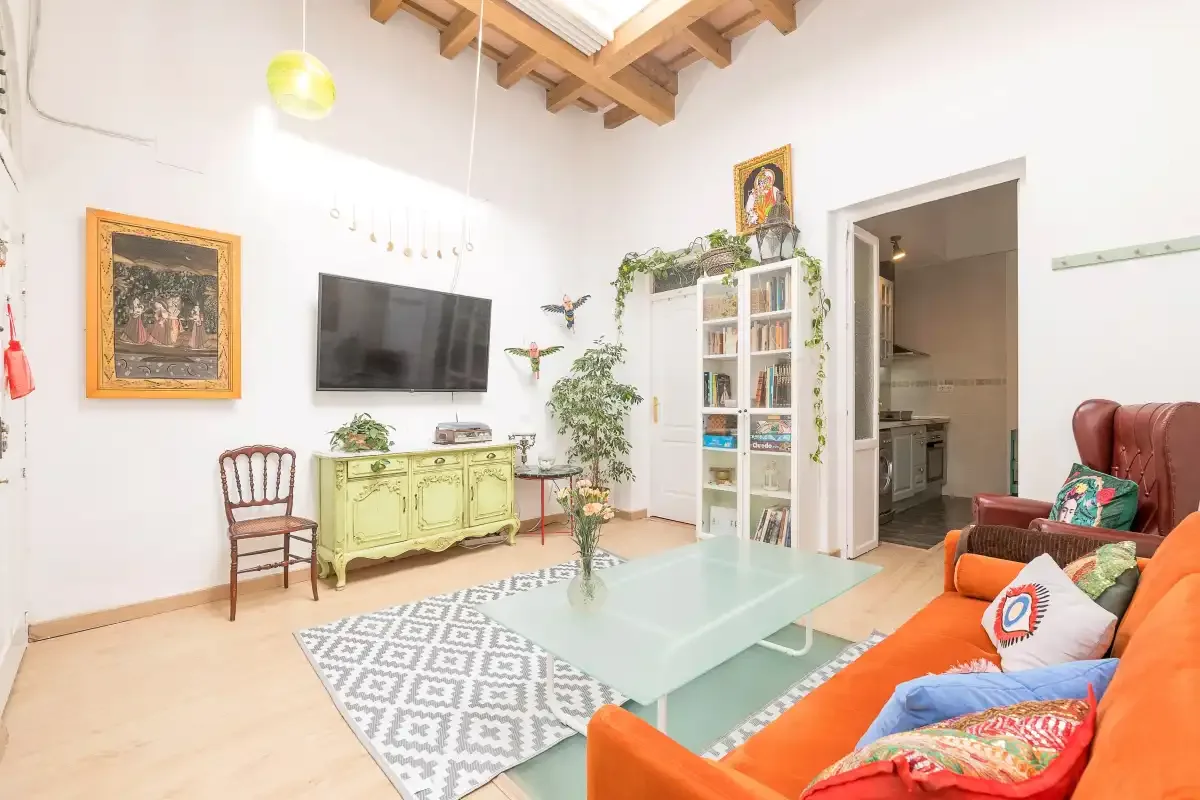 A bright living room with colorful seating, a glass coffee table, and a bookcase.