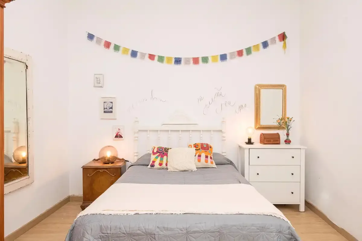A bedroom with a double bed, colorful pillows, and a dresser.