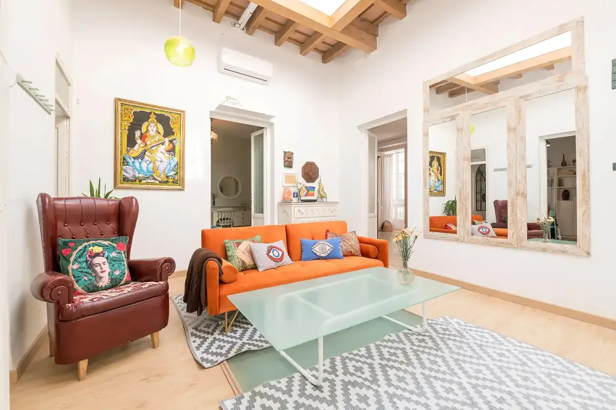 A bright living room with orange seating and a glass coffee table.