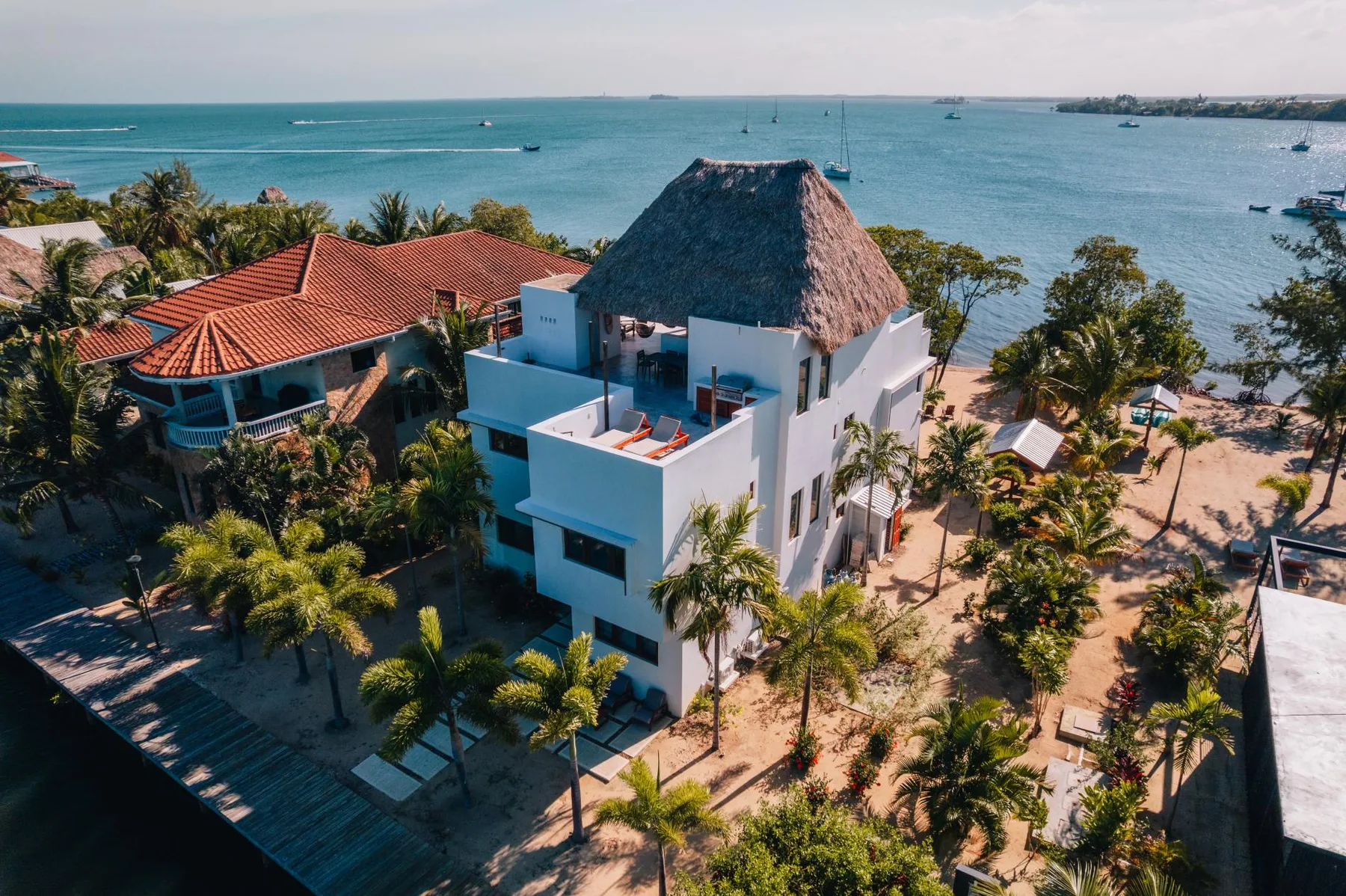 Aerial view of a white seaside building with palm trees beside the water.