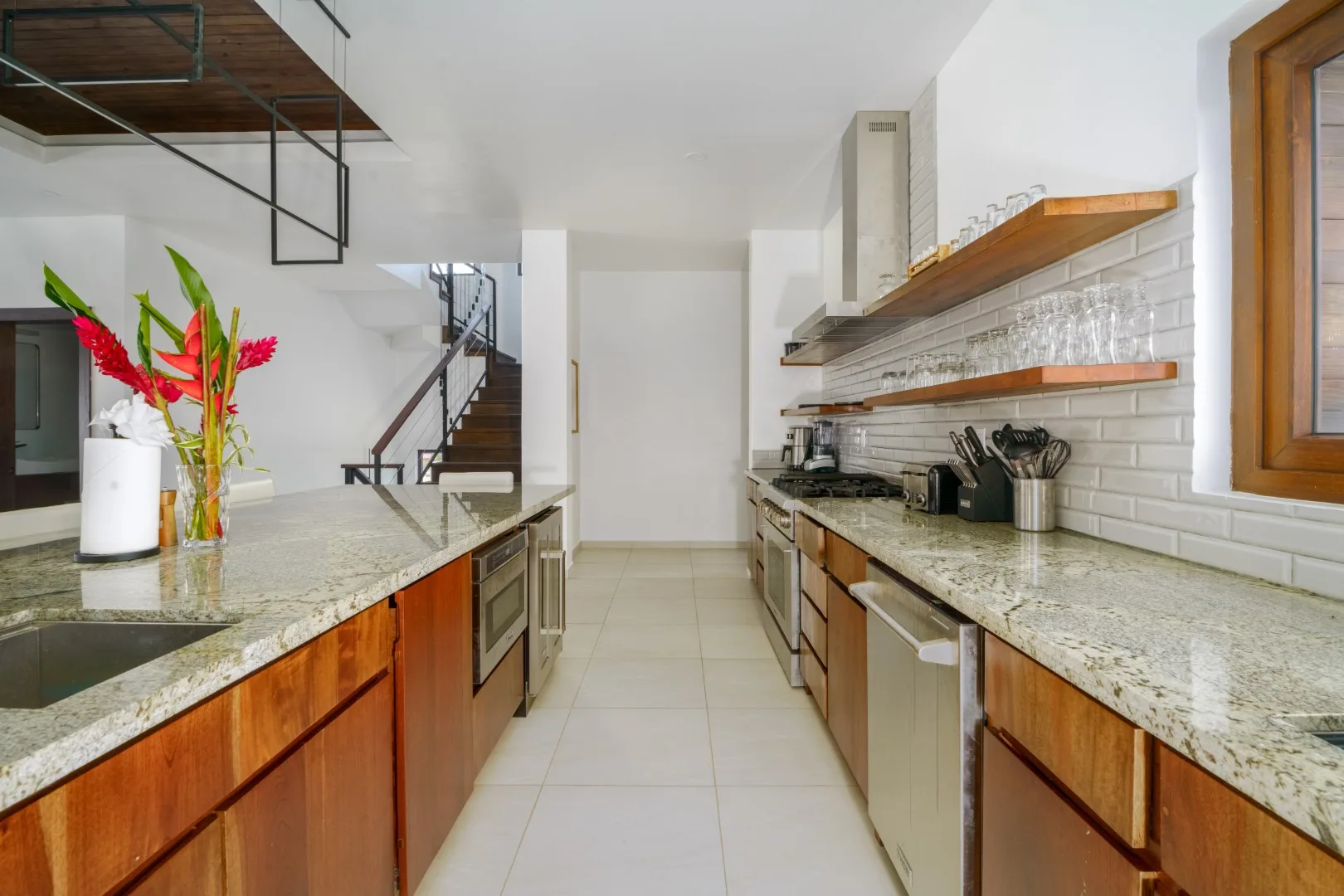 A bright kitchen with long counters, wooden cabinets, and open shelving.