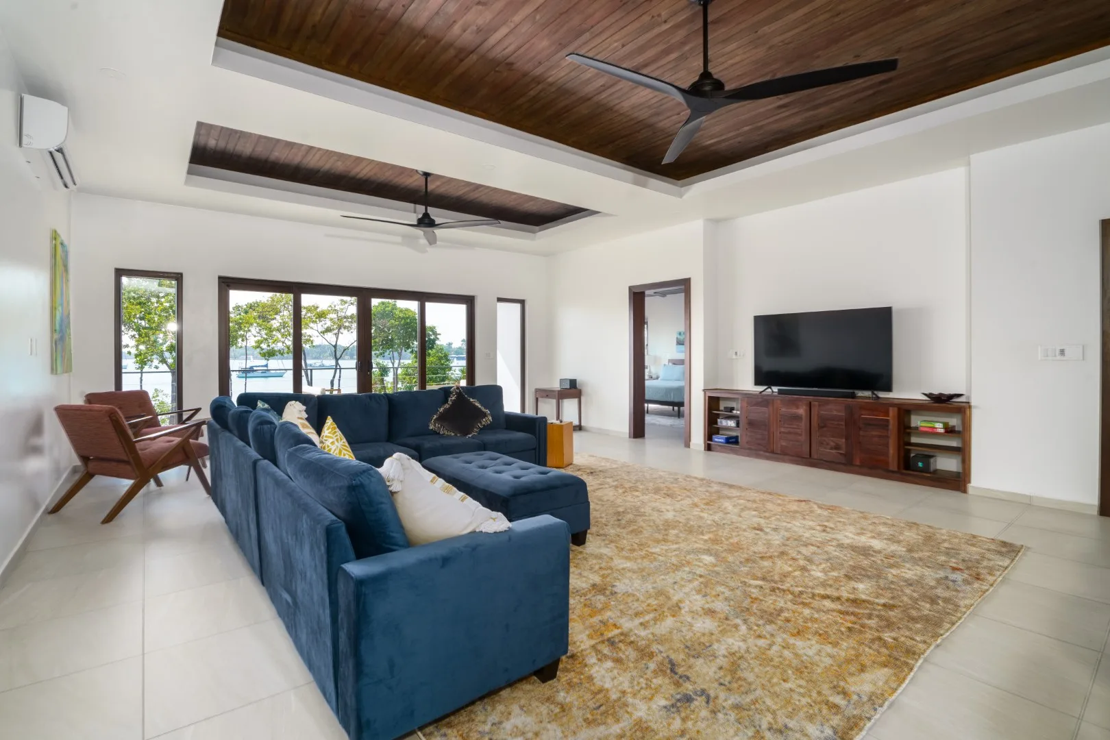 A bright living room with blue seating, a television, and large windows.