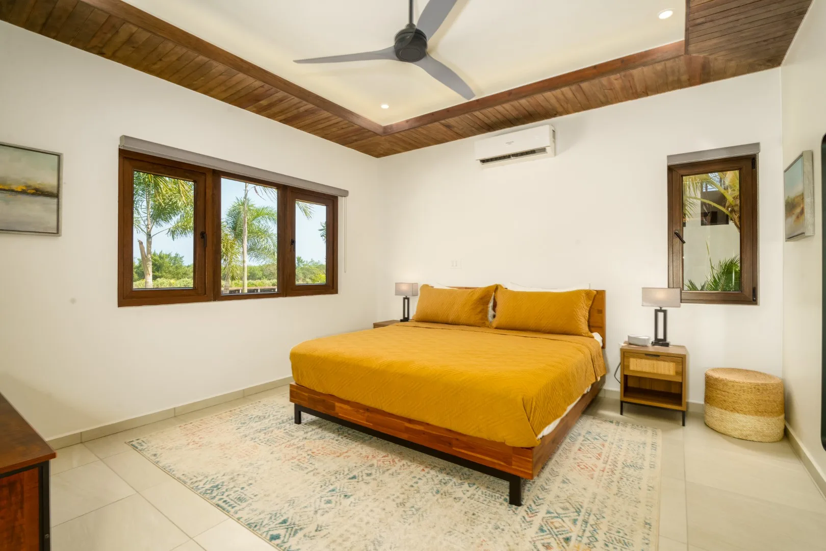 A bedroom with a mustard-colored bed beneath a ceiling fan.