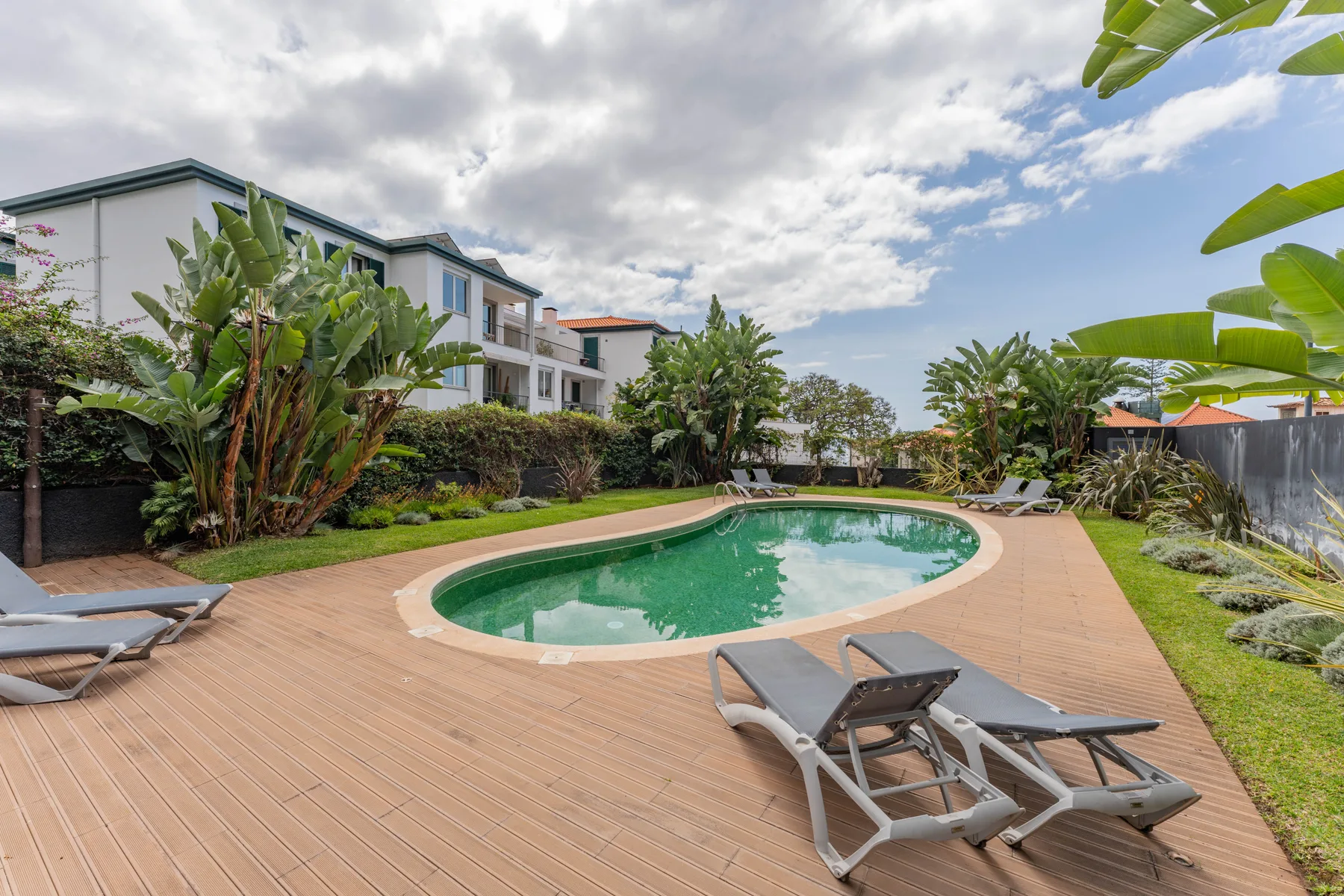 Una piscina está junto a una terraza de madera y asientos para descansar.