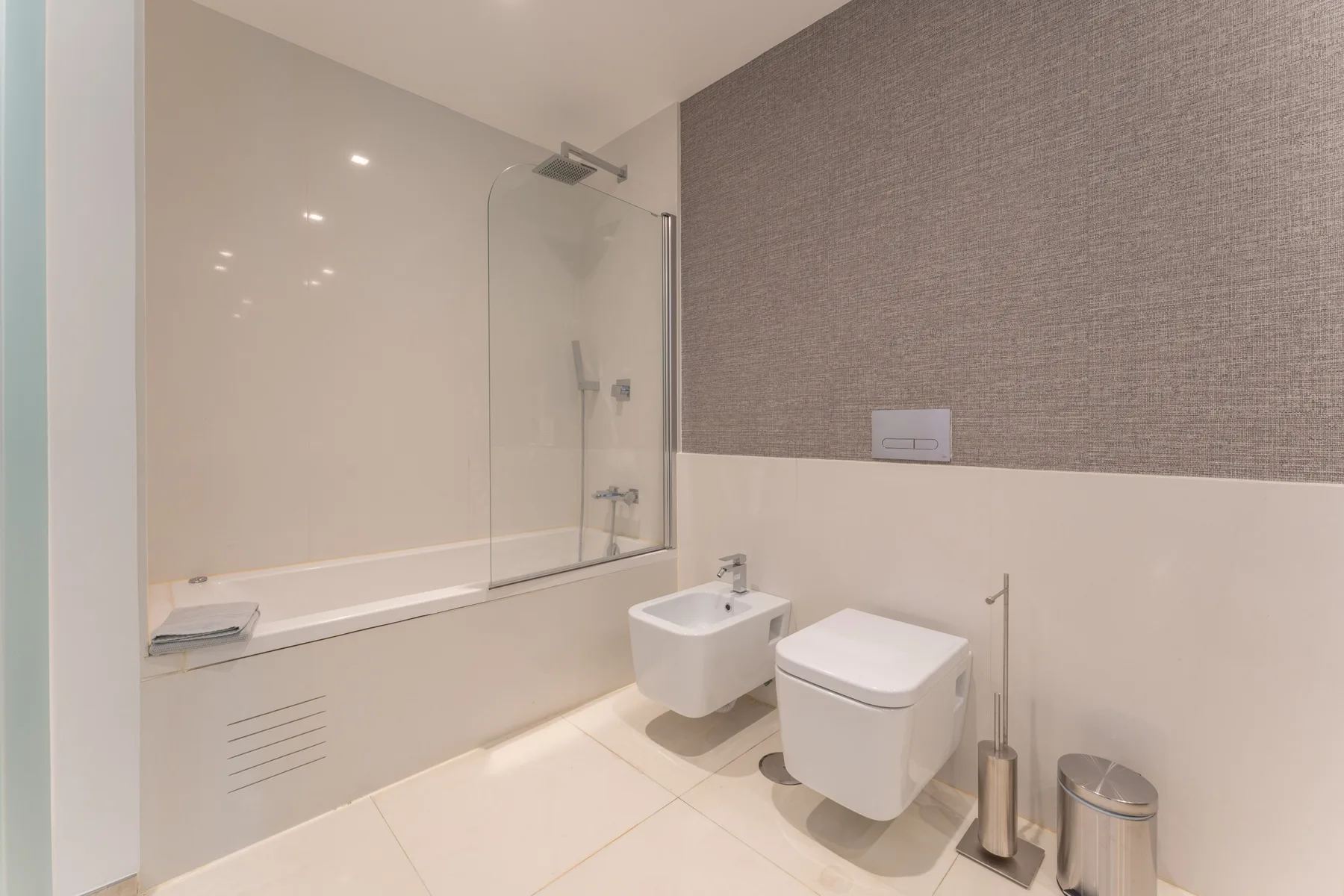 Un baño con bañera, mampara de vidrio y accesorios montados en la pared.