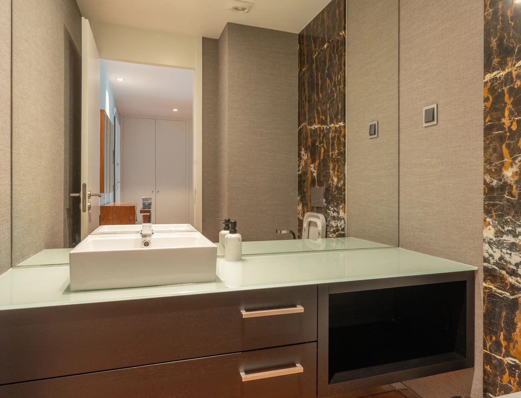 Un lavabo de baño aparece debajo de un gran espejo de pared.