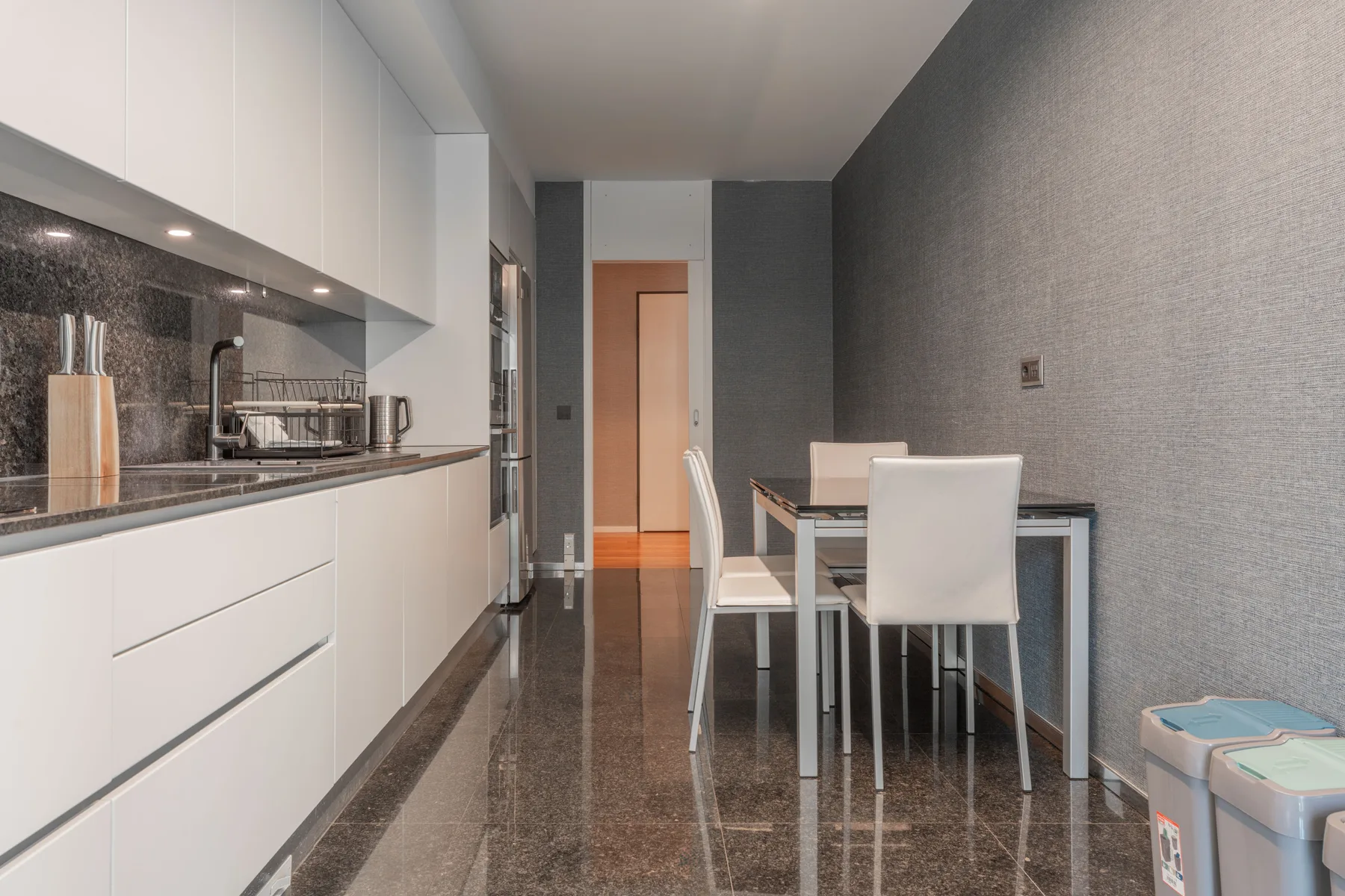 Una cocina moderna y zona de comedor con armarios blancos y una mesa.