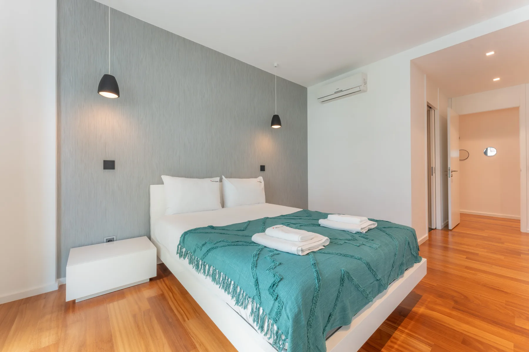 Dormitorio con una cama vestida con ropa de cama verde azulado y una pared gris.