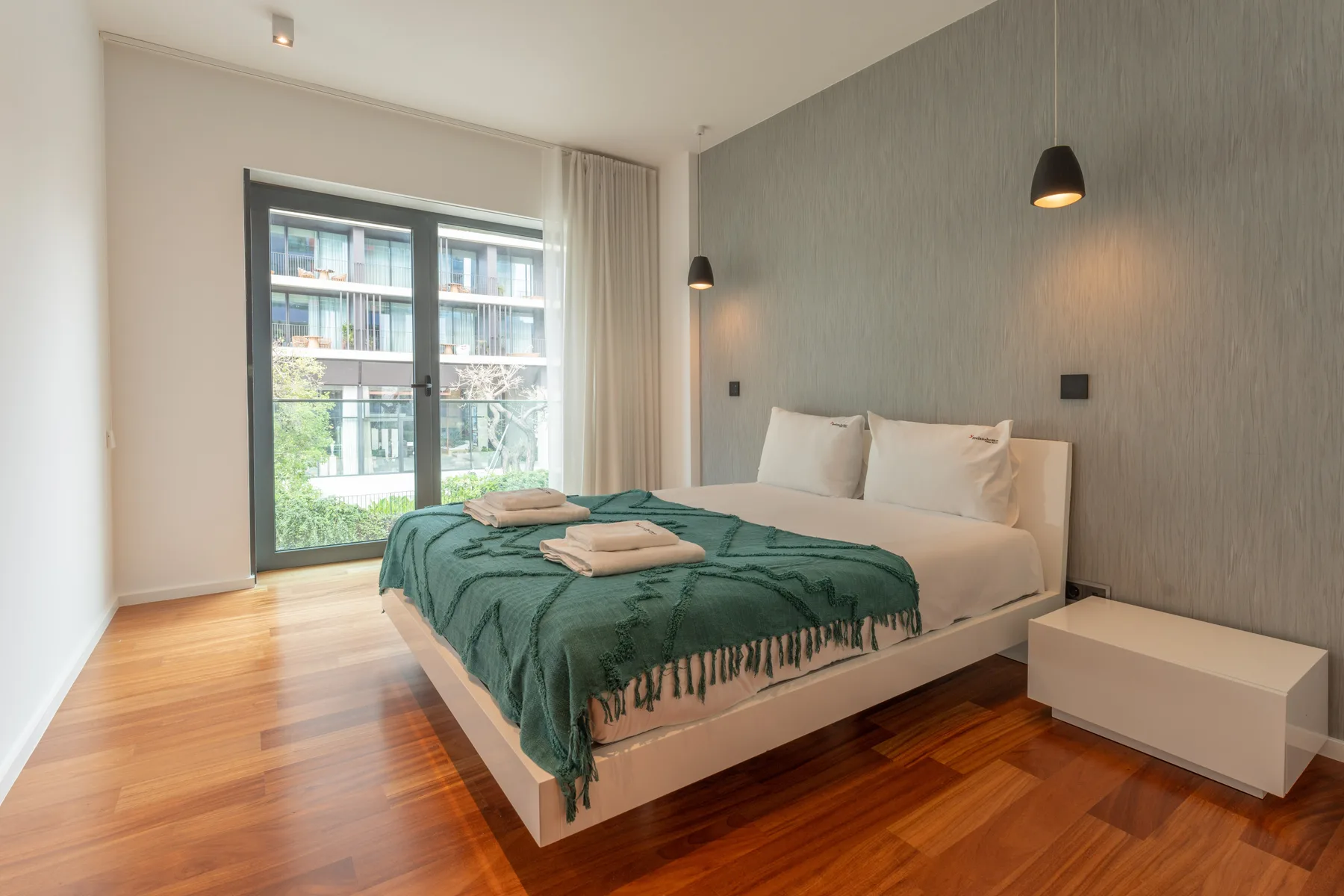 Un dormitorio con una cama cubierta con una manta verde junto a una ventana amplia.