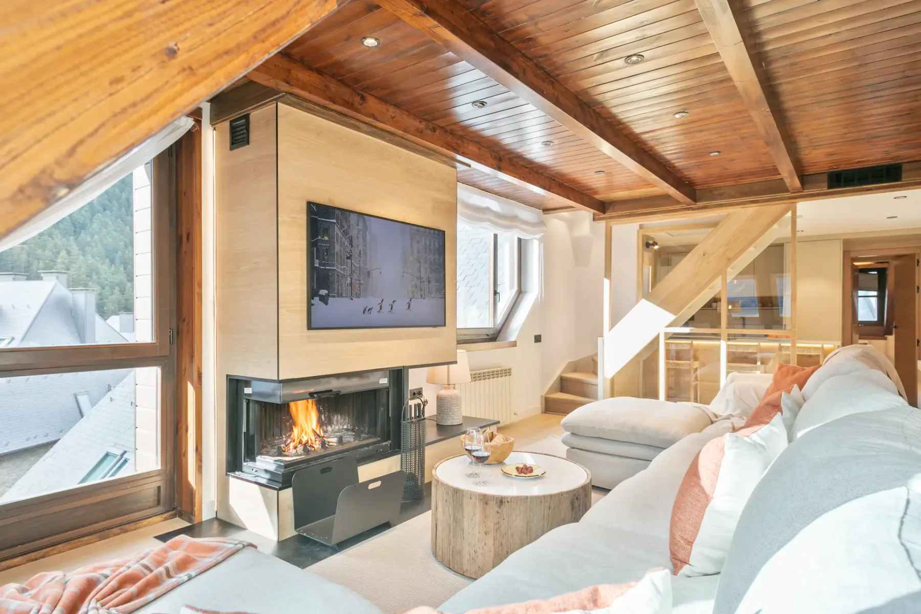 A living room with a fireplace, television, and light-colored seating beneath a wood-paneled ceiling.