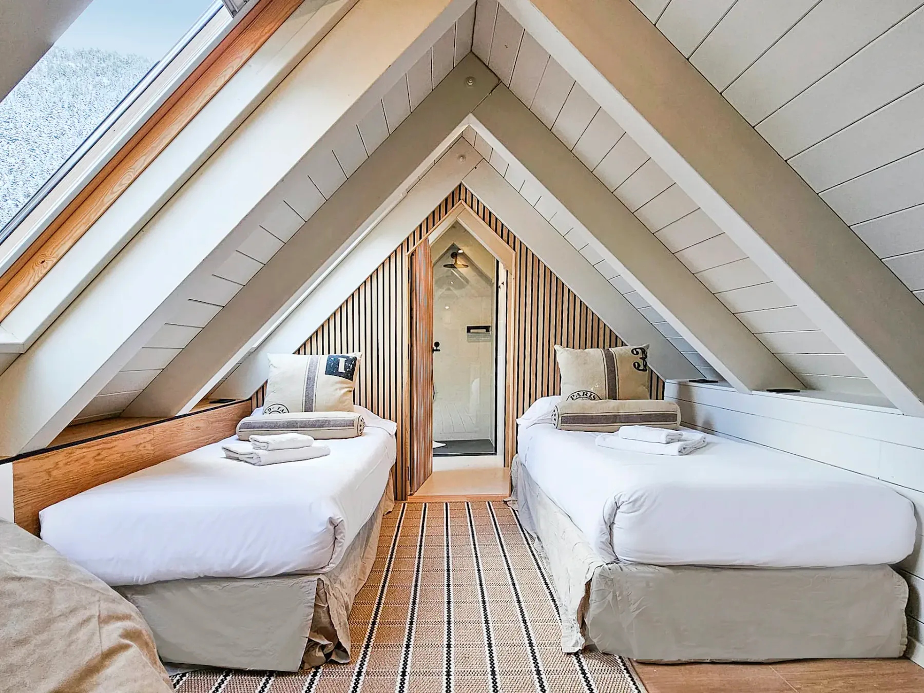 An attic bedroom with two beds beneath a sloped ceiling and a skylight.