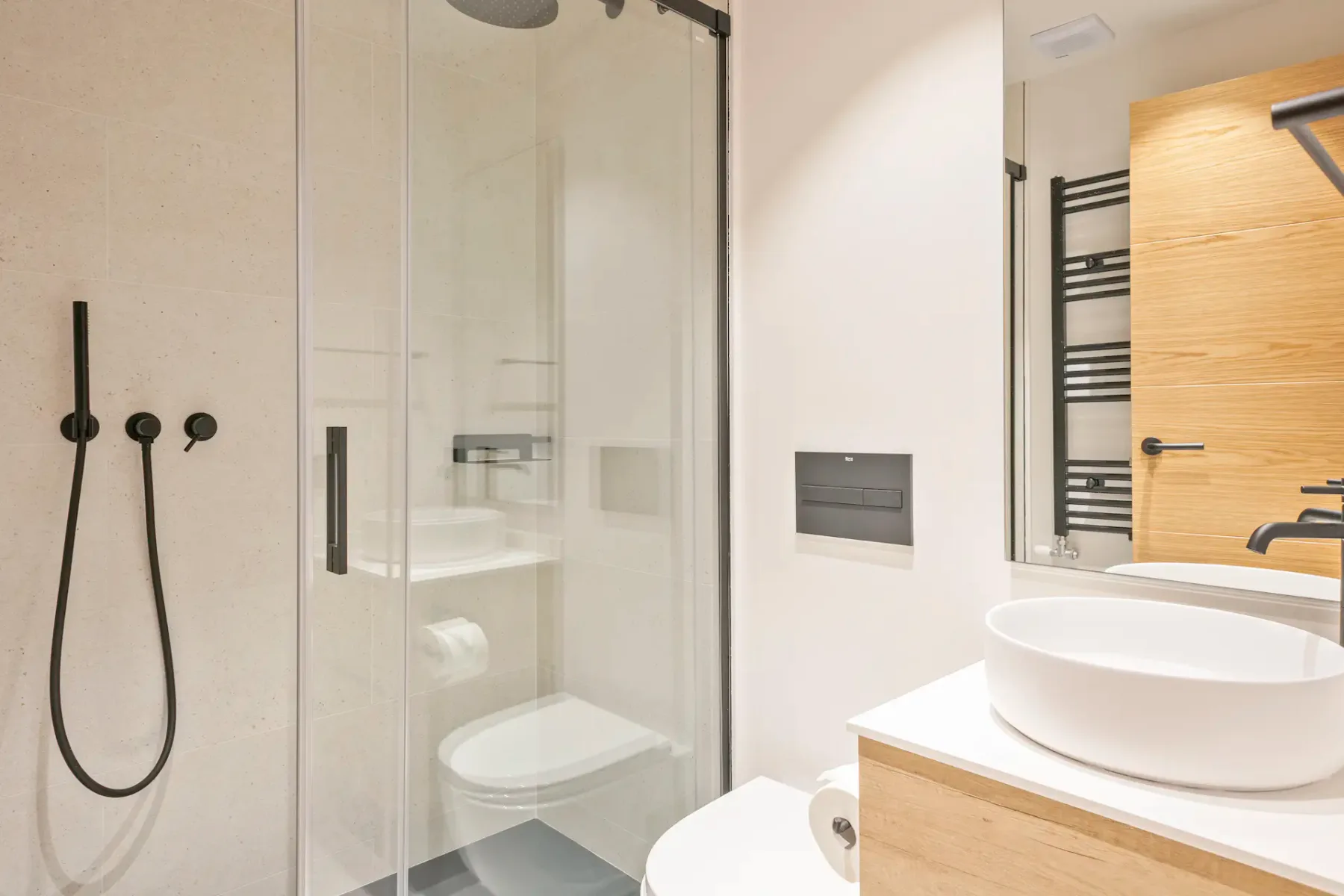 Modern bathroom with a glass shower, wall-mounted toilet, and vessel sink on a wood vanity.