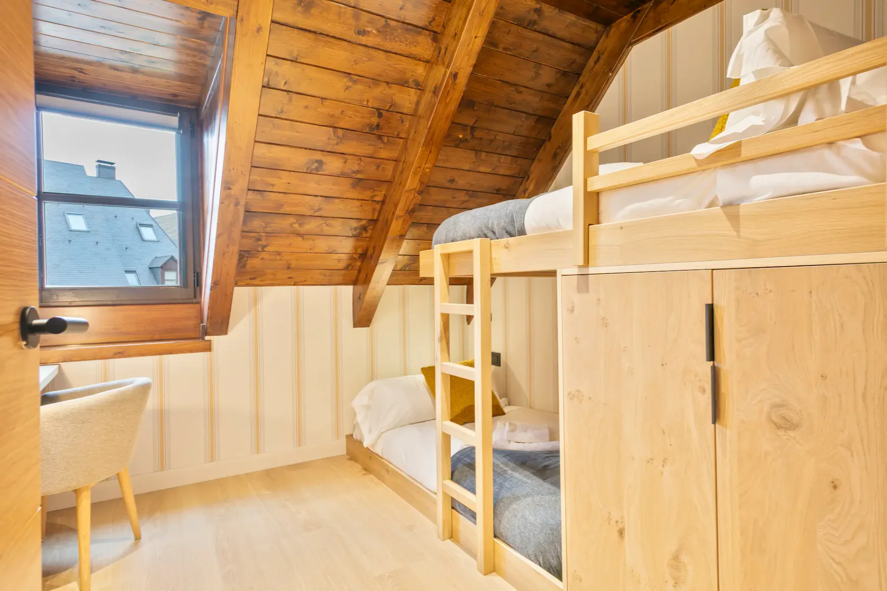 A compact bedroom with built-in bunk beds beneath a sloped wooden ceiling.