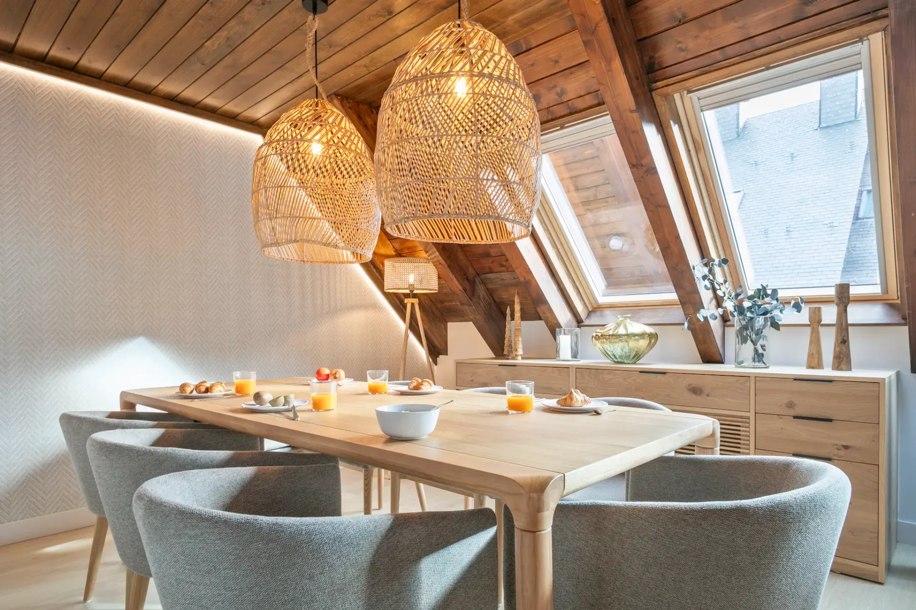 A dining area with a wooden table and upholstered seating beneath sloped wooden ceilings.