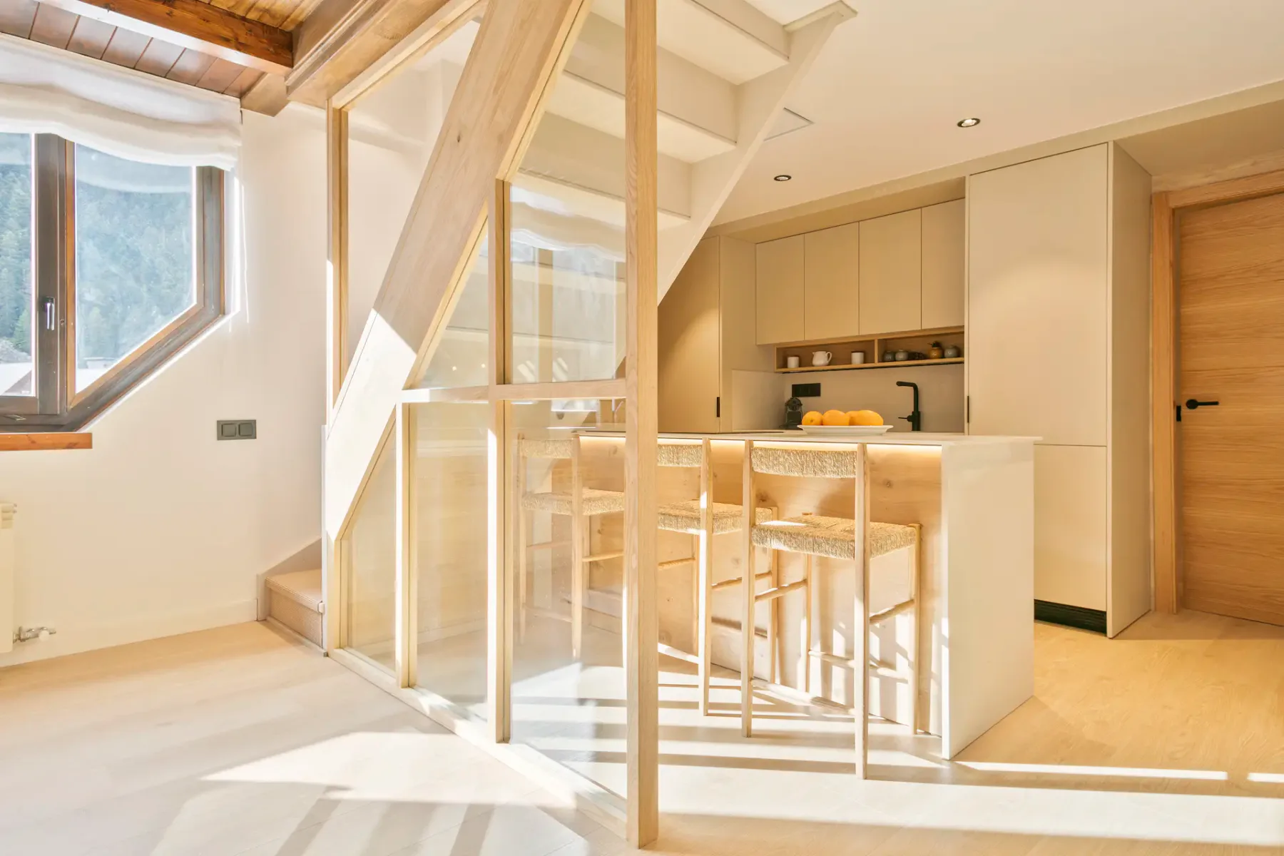 A bright kitchen with a central island and stools beneath exposed wooden beams.