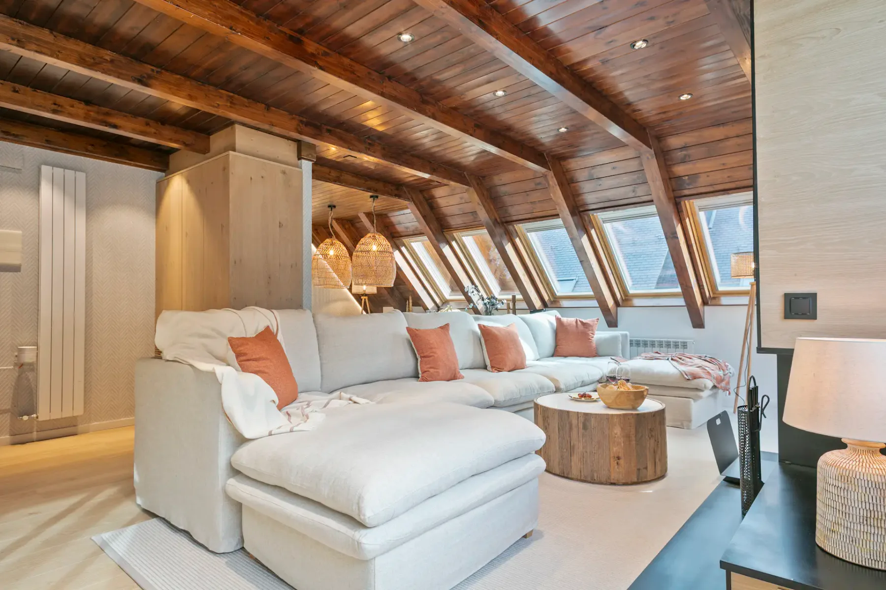 A bright living room with sectional seating beneath a sloped wooden ceiling and skylights.
