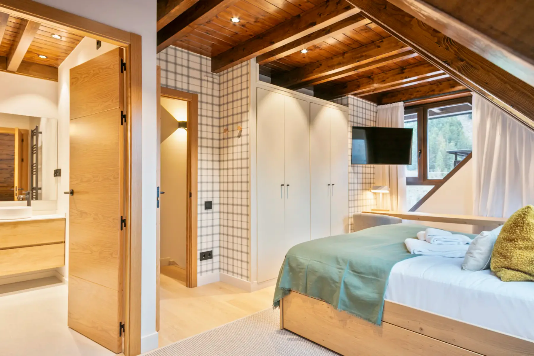 A bedroom beneath a sloped wooden ceiling, with a bed and built-in cabinets.