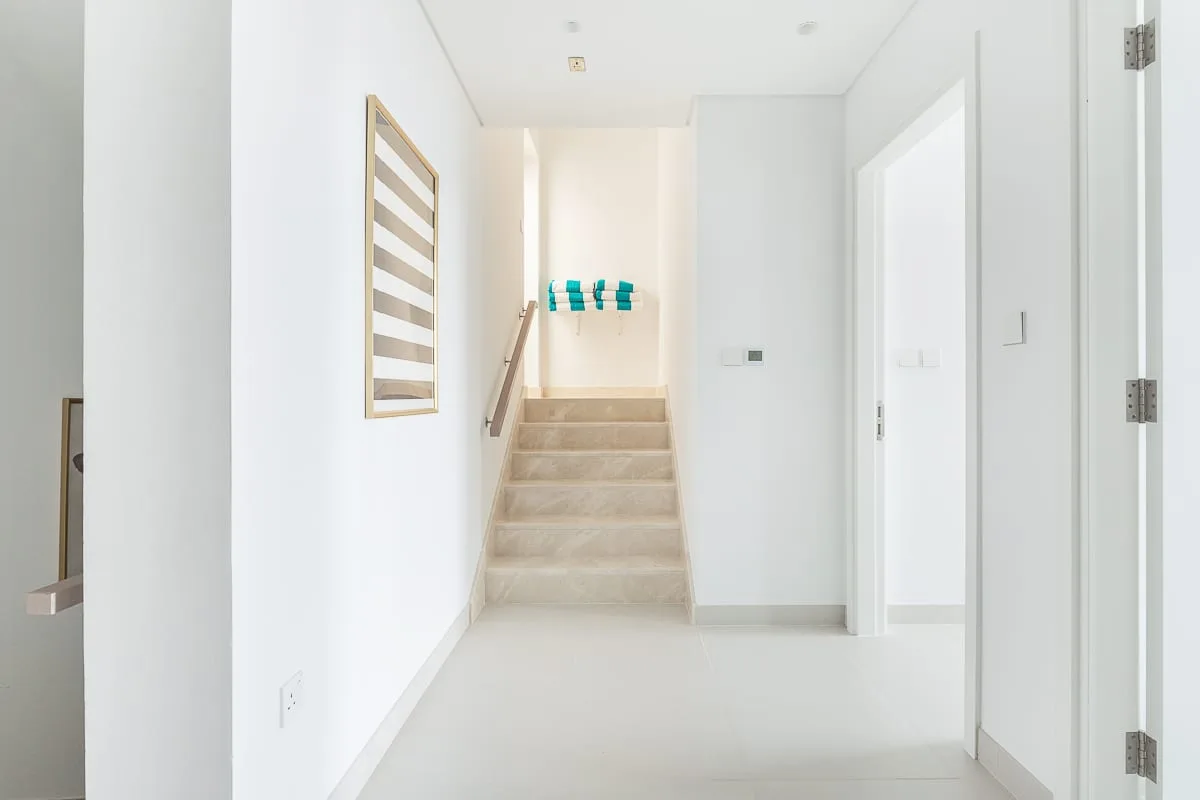 Un pasillo blanco y luminoso conduce a una escalera corta con pasamanos.