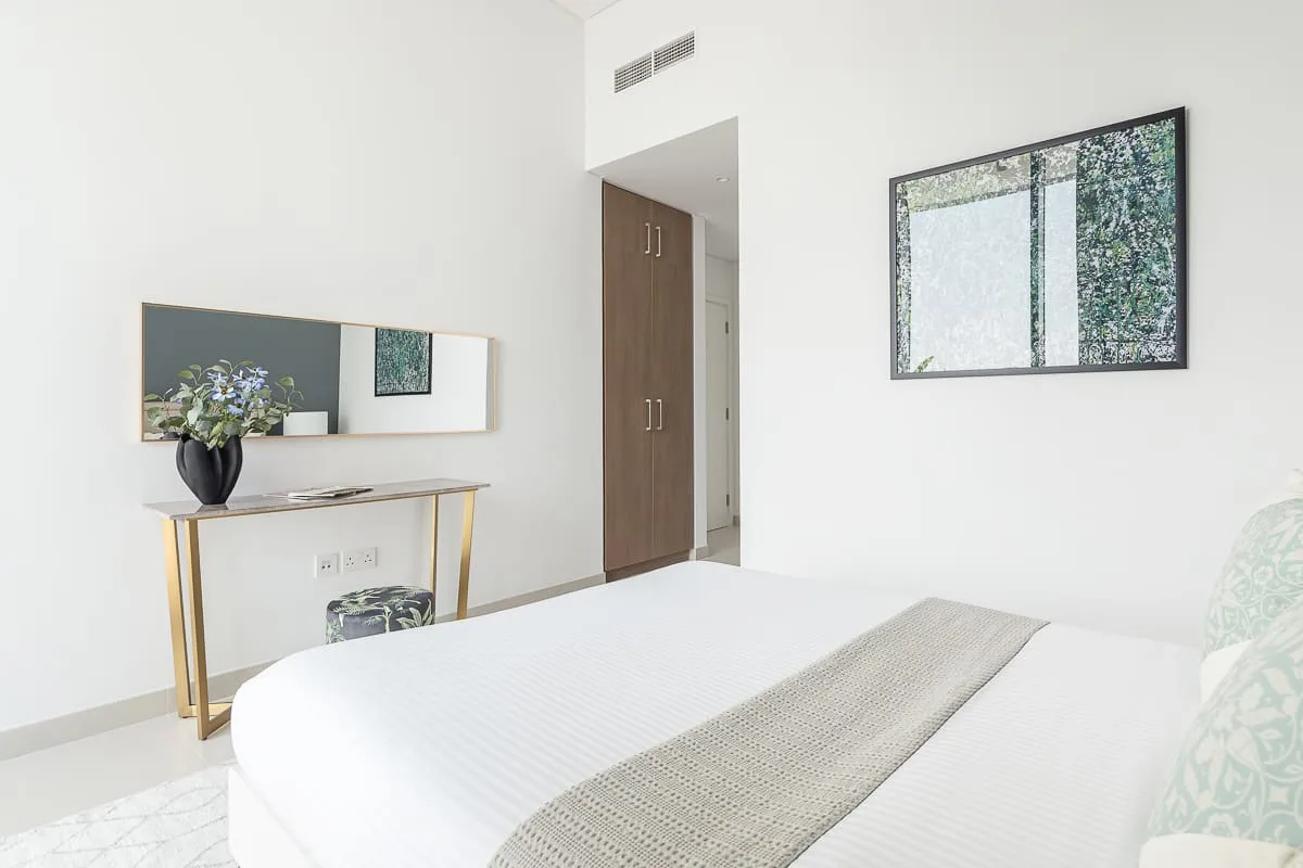Un dormitorio luminoso con ropa de cama blanca y un cuadro en la pared.
