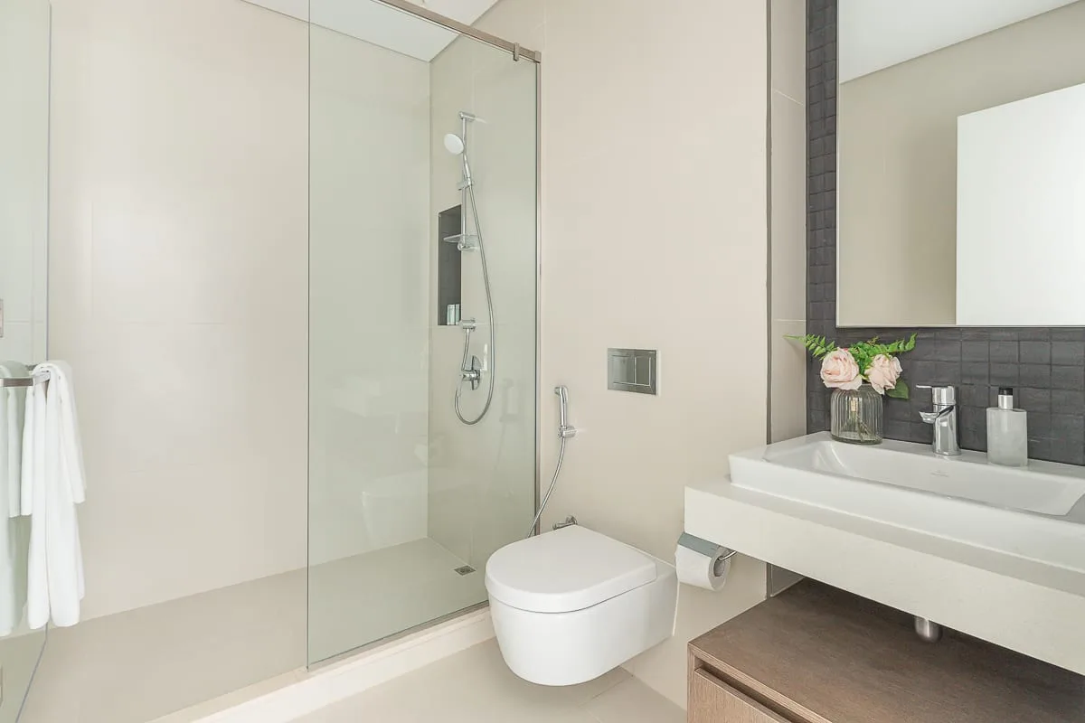 Un baño moderno con ducha de vidrio, inodoro suspendido y lavabo.