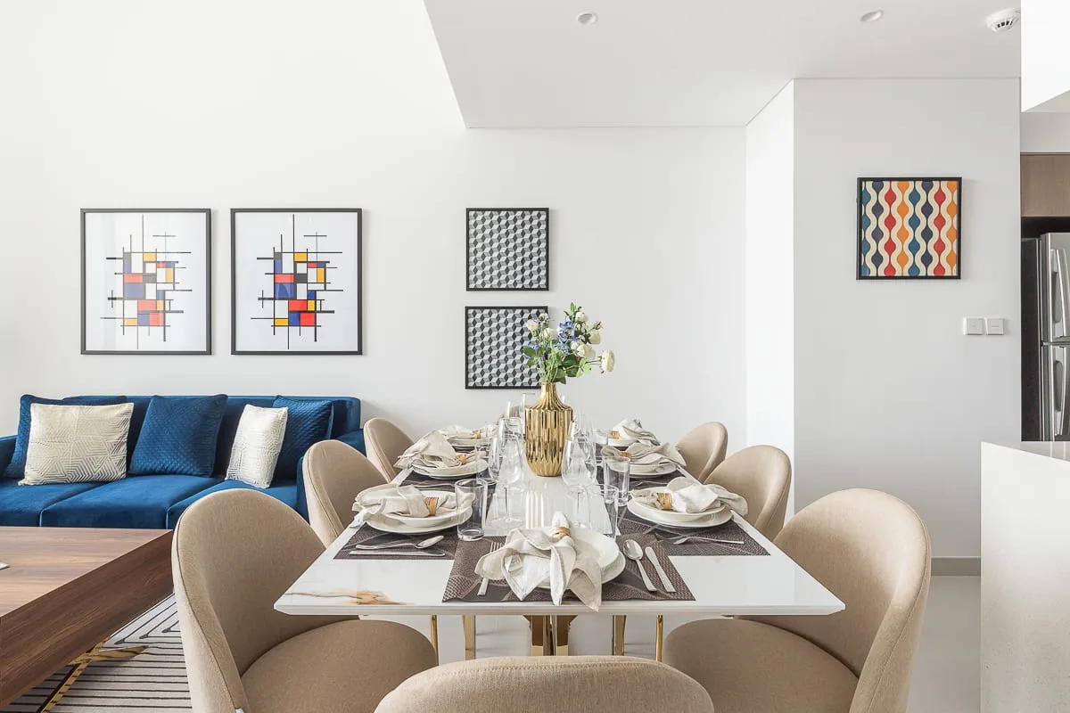 Un comedor luminoso con la mesa puesta junto a una zona de estar azul.