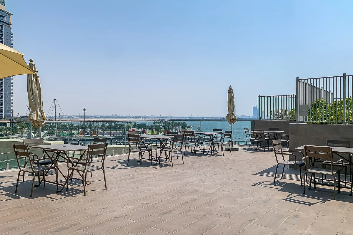 Una terraza de comedor en la azotea da al agua, con mesas y sillas distribuidas por la plataforma.