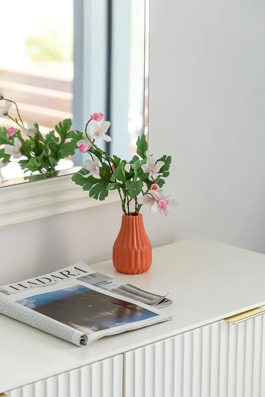 Una mesa junto a una ventana tiene un jarrón con flores y una revista.