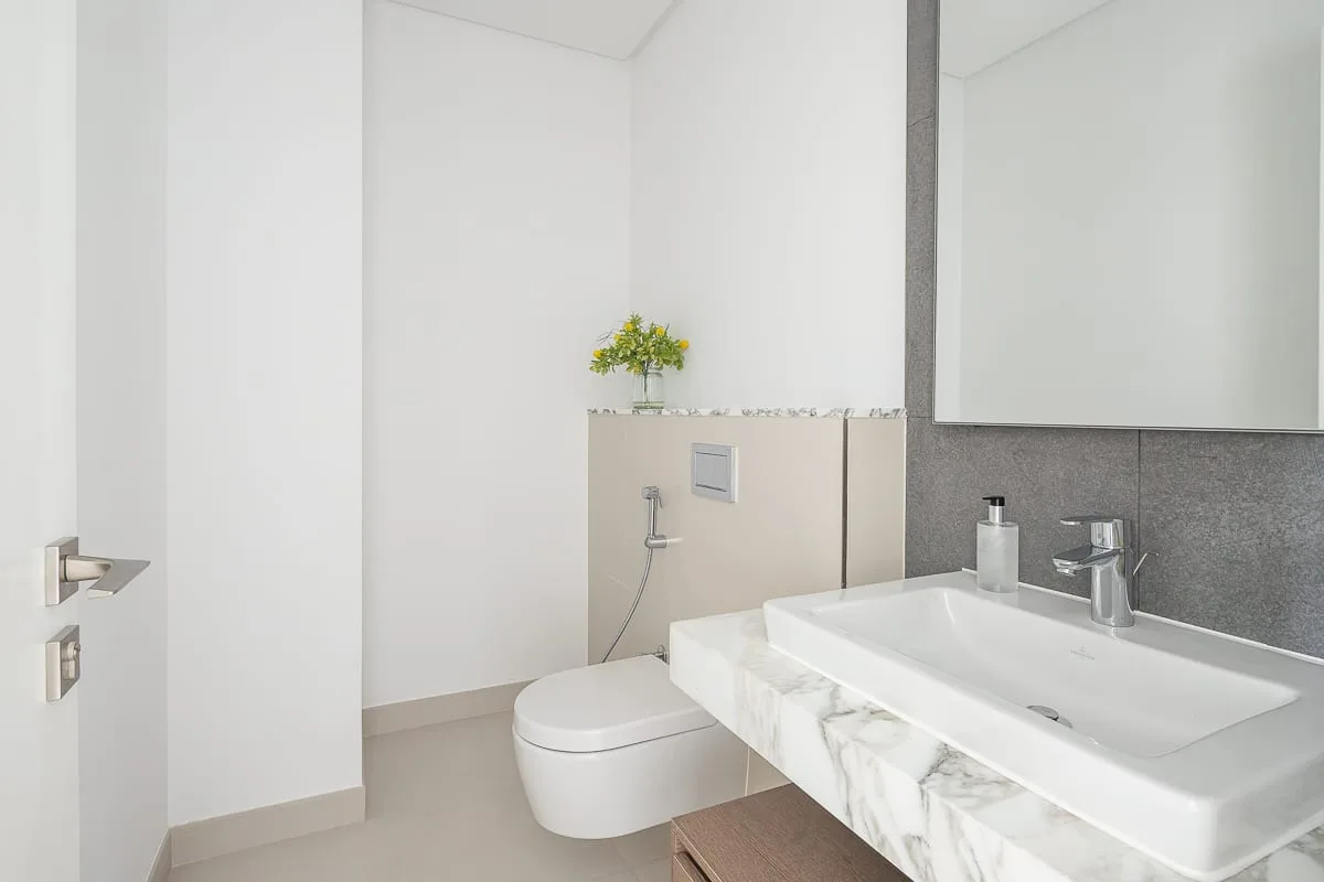 Un baño luminoso con un inodoro y un lavabo blanco bajo un espejo grande.