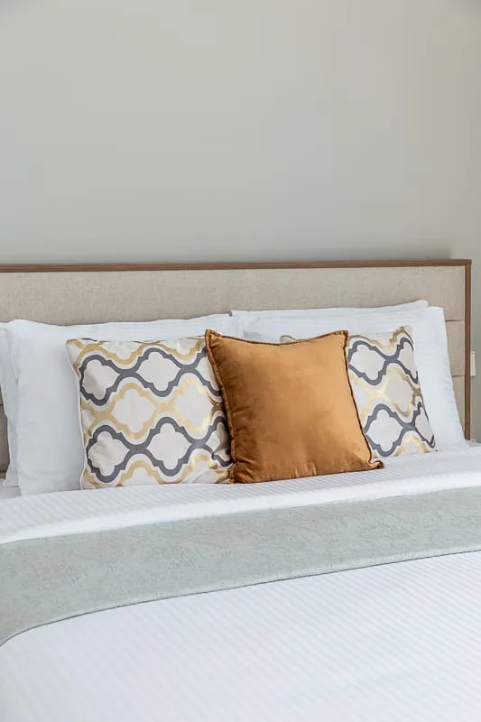 Una cama bien tendida con almohadas estampadas y un cojín decorativo color óxido.