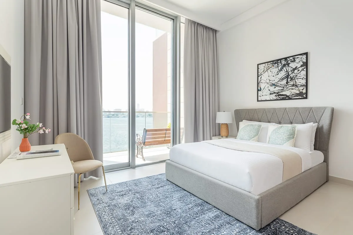 Dormitorio luminoso con una cama junto a grandes puertas de cristal que dan a un balcón.