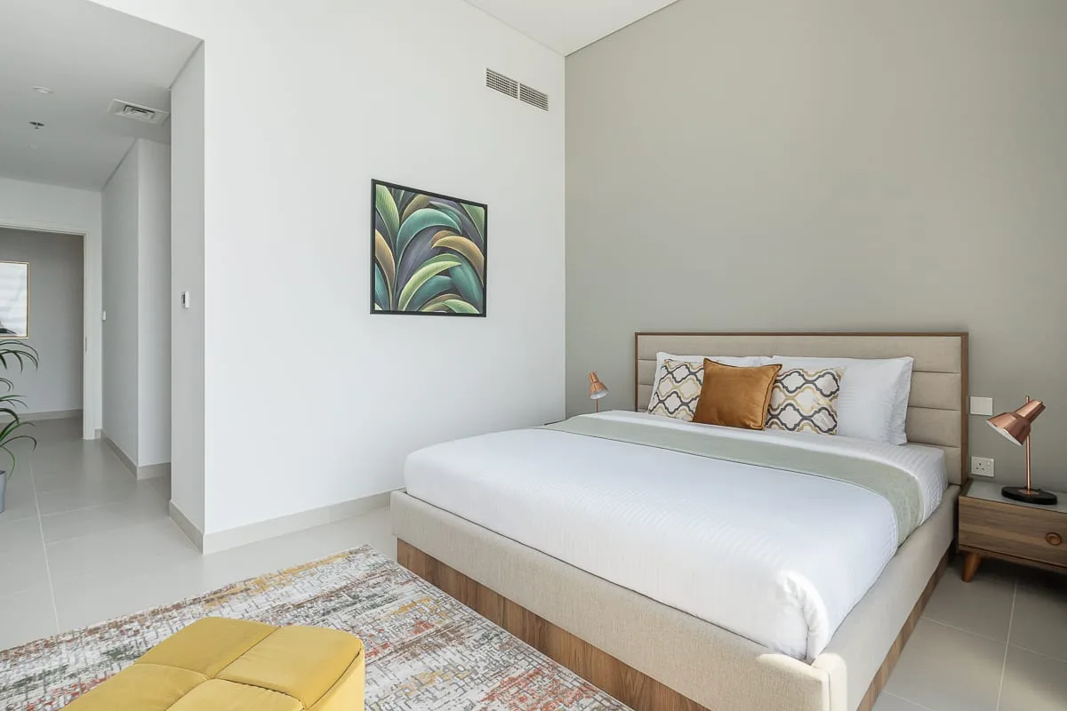 Un dormitorio luminoso cuenta con una cama bien tendida y arte abstracto colorido en la pared.