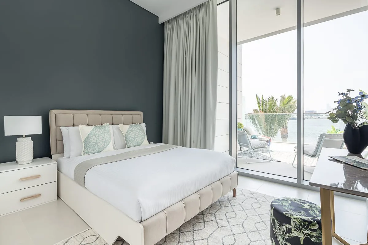 Un dormitorio luminoso con una cama bien tendida junto a grandes puertas de vidrio.