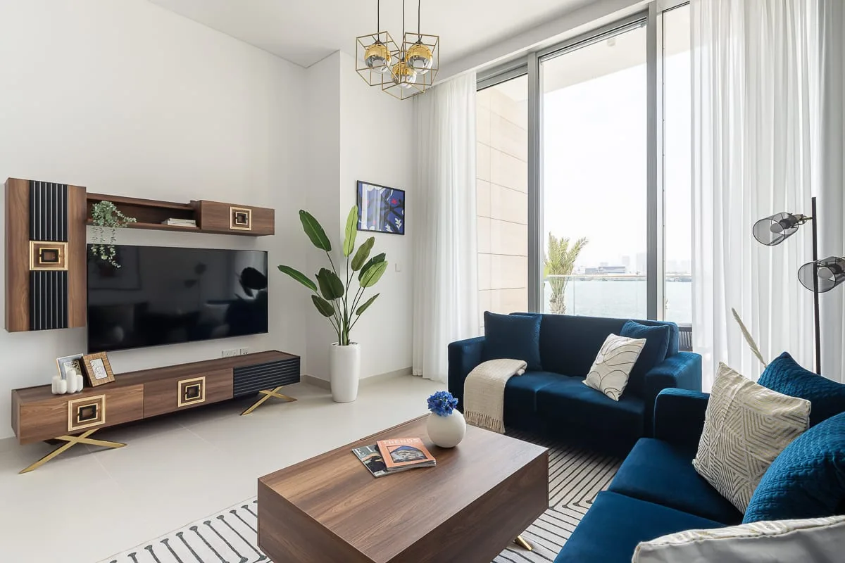 Una sala luminosa con asientos azules, una mesa de centro de madera y grandes ventanas.