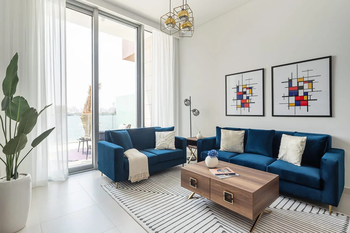 Una sala luminosa con asientos azules, una mesa de centro baja y arte abstracto en la pared.