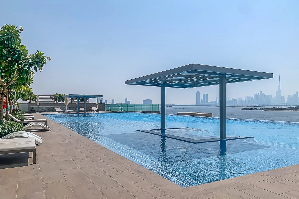 Una piscina al aire libre tiene una plataforma sombreada y tumbonas junto al borde.