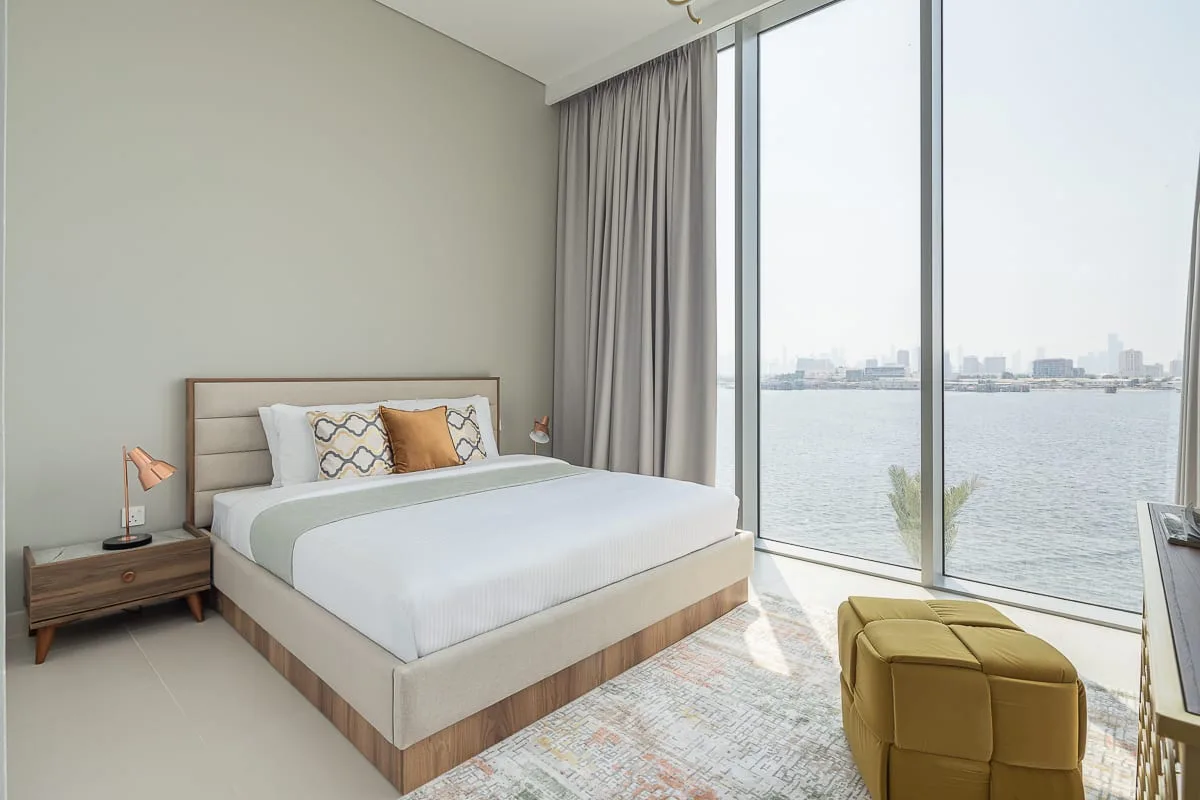 Un dormitorio con una cama junto a una gran ventana con vista al agua.