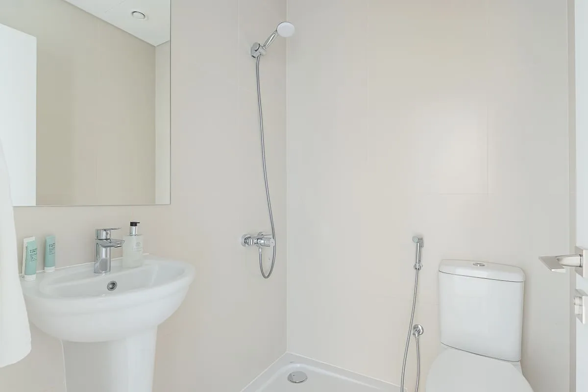 Un baño luminoso con lavabo, espejo, ducha e inodoro.