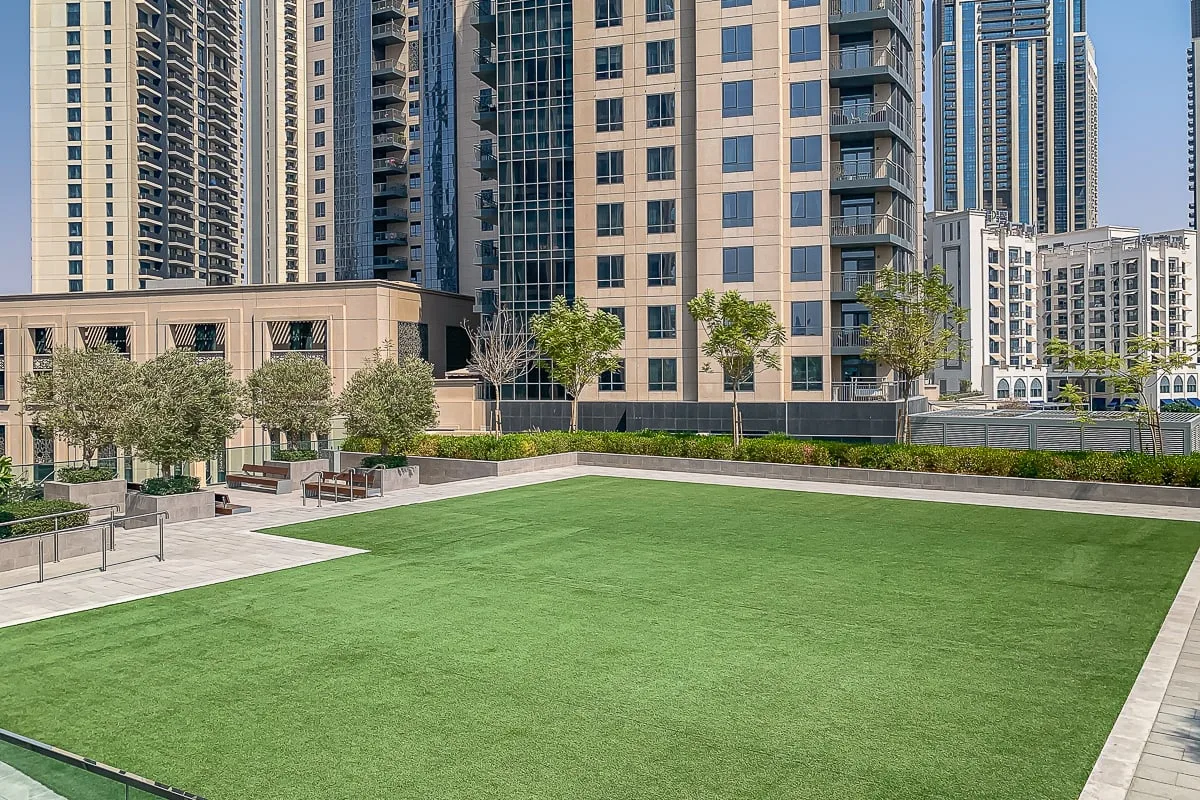 Un patio ajardinado al aire libre con césped verde, árboles y edificios altos.